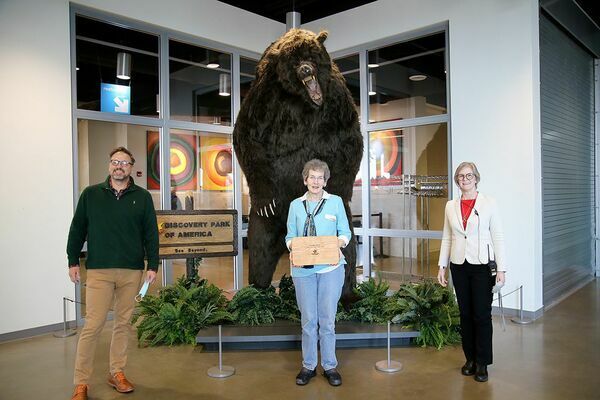 Sue Ellen Morris, center was the recipient of the 2020 Volunteer of the Year award. Presenting her with a handmade serving board, made by volunteer John R. Hall, was Discovery Park’s president and CEO Scott Williams and director of education Polly Brasher. (Photo submitted)